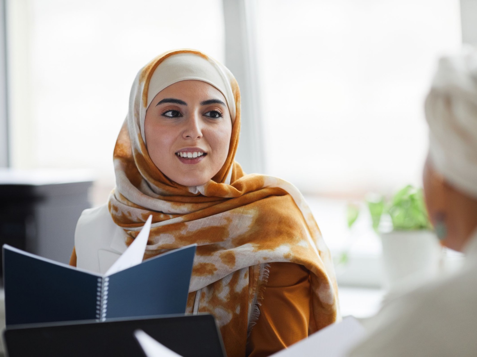 A woman listening during a conversation, an open notebook resting in front of her.