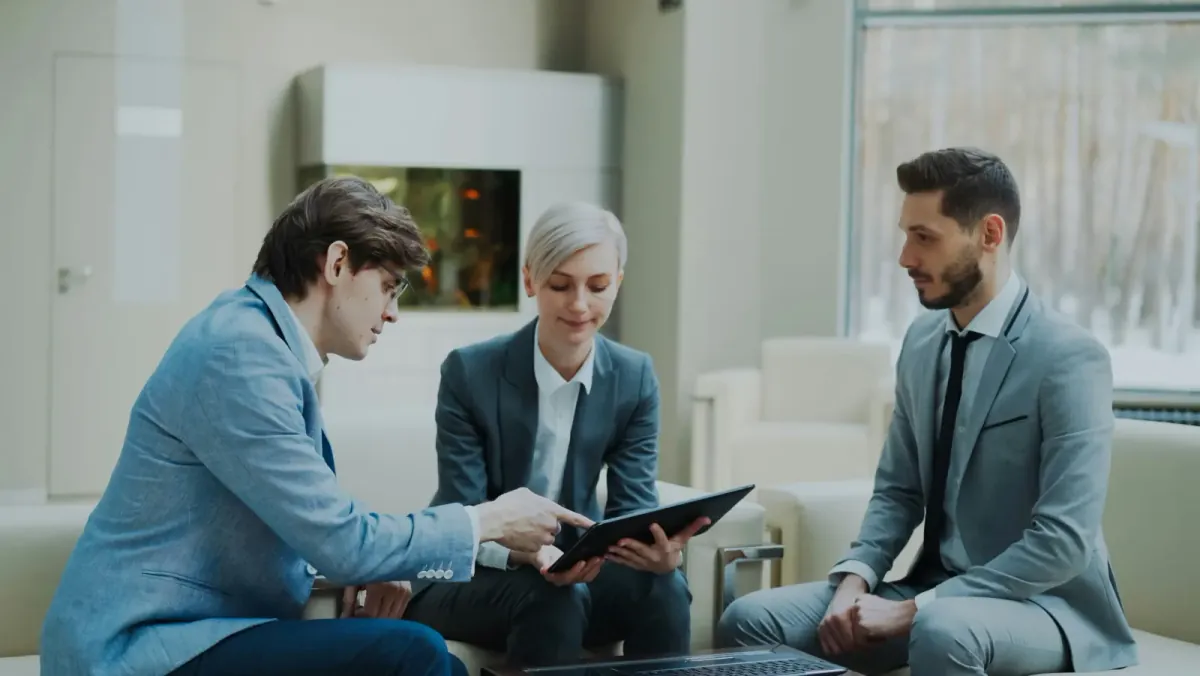 An agent leaning in to point something out on a tablet while two colleagues on a sofa listen.