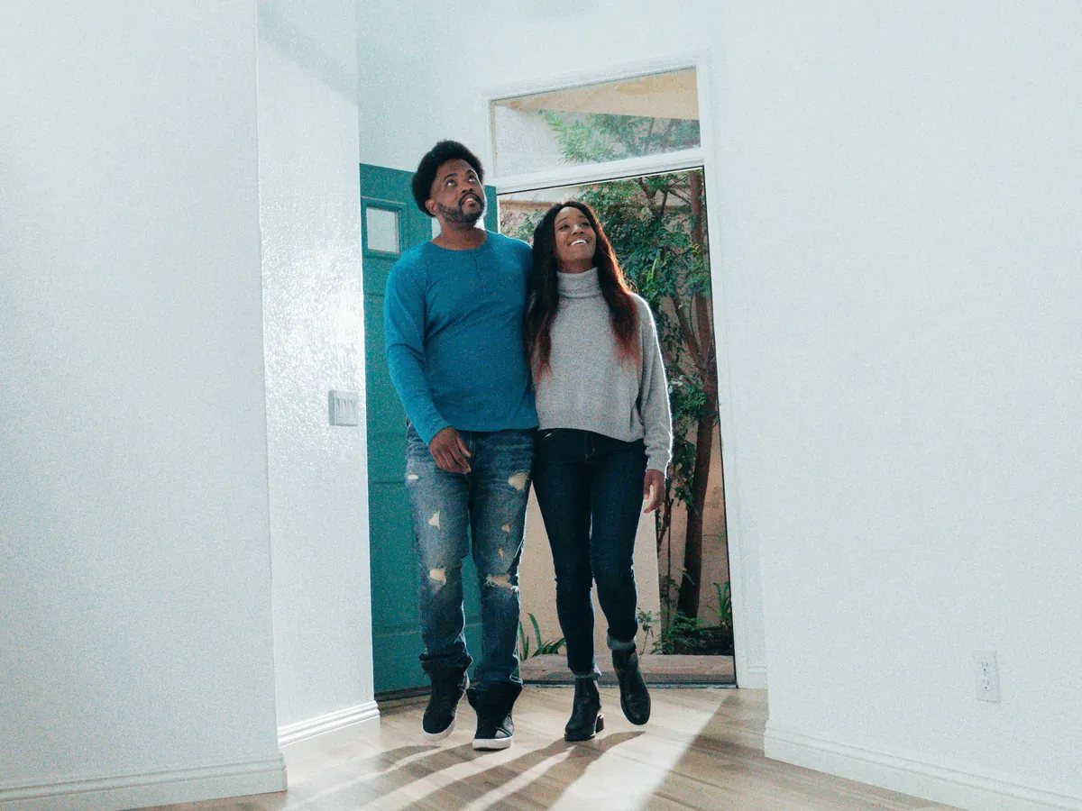 A couple step through the front door of an empty home, looking up and around as they take it in.