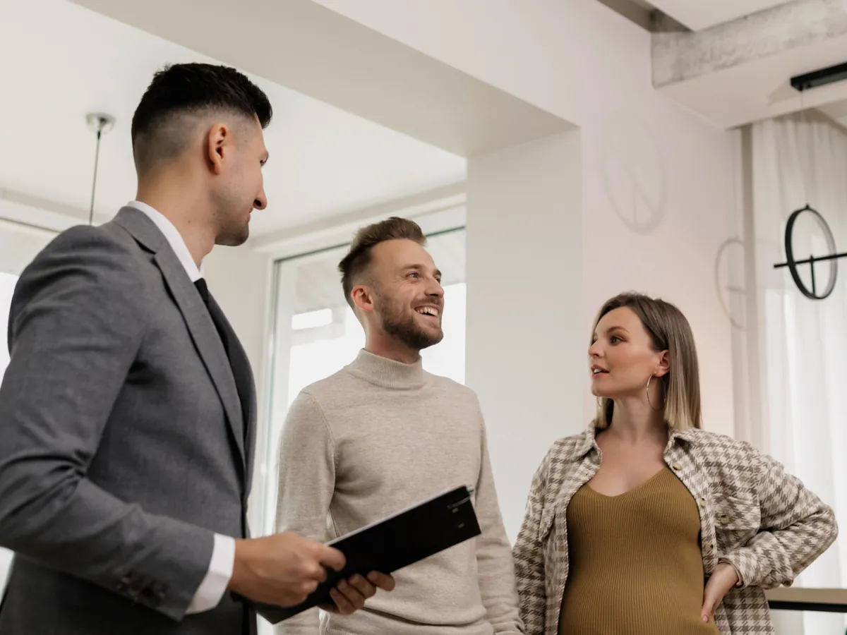 A couple talk with their agent during a viewing, the man smiling and the woman asking a question.