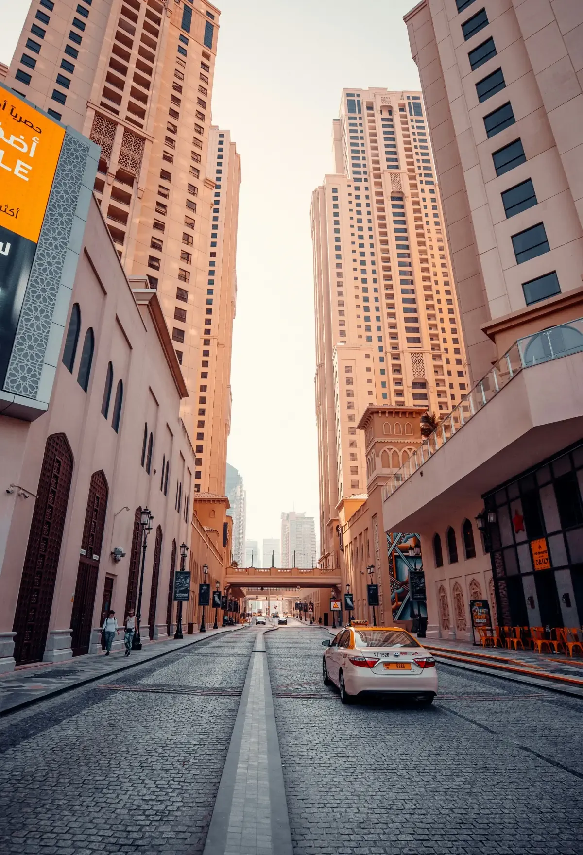 Towers rising either side of a cobbled street in Dubai Marina, a taxi driving between them.