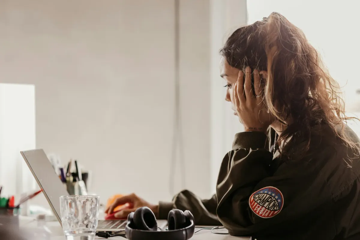 A woman at her desk, head resting in her hand, reading something on her laptop.