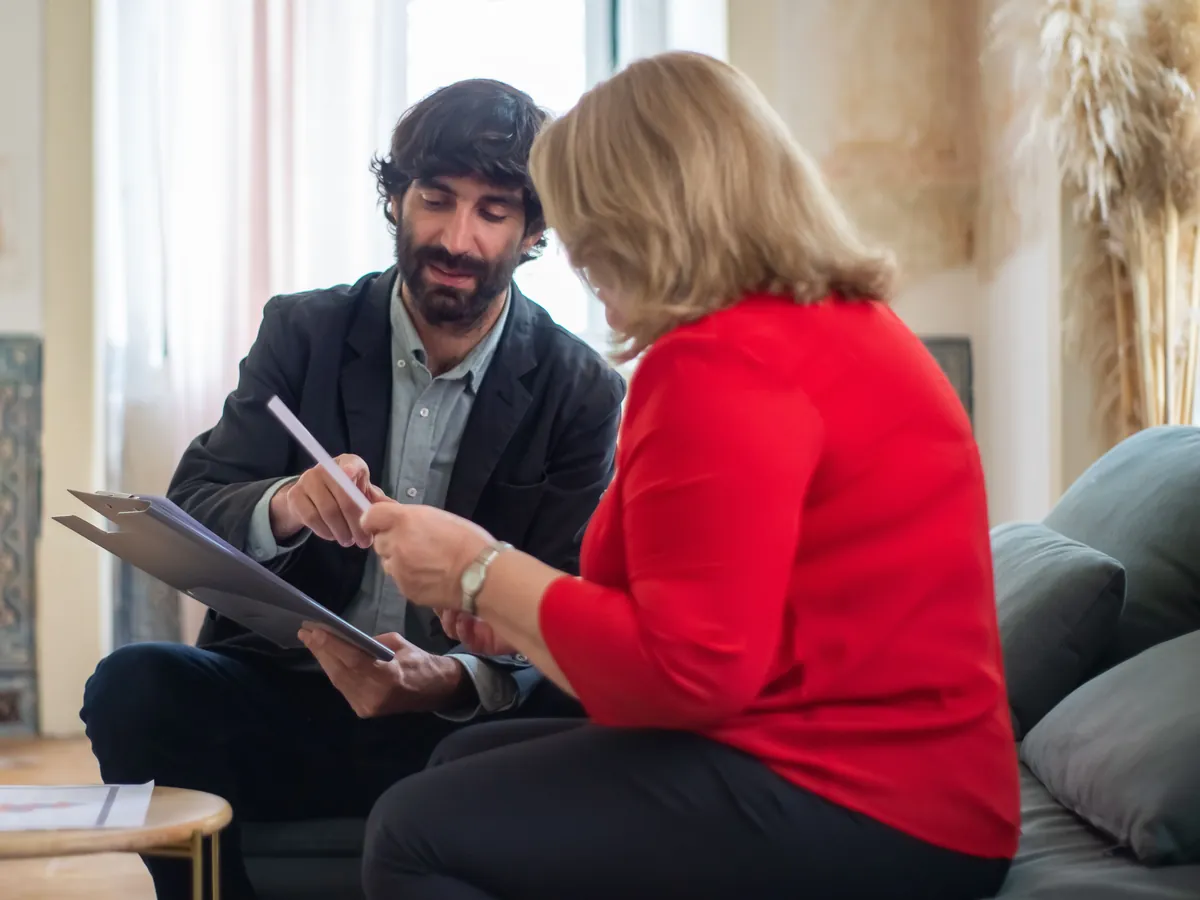 A homeowner and an adviser sit side by side on a sofa, going over a sheet of paper together.